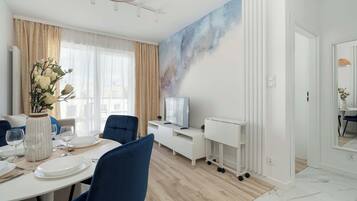 Un'area pranzo moderna con un tavolo bianco apparecchiato per quattro persone, sedie blu, un vaso con fiori bianchi e un grande quadro appeso al muro.