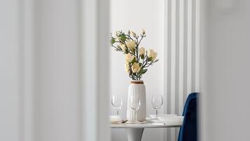 A dining area with a white table, two blue chairs, a white vase with flowers, and a pendant light.