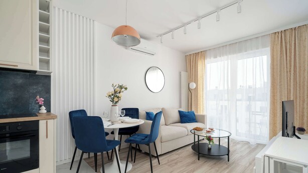 Un salon moderne comprenant un canapé, une table à manger, des chaises, une table basse, un téléviseur et un coin cuisine avec un four.