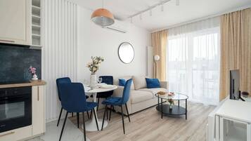 A modern living room with a sofa, dining table, chairs, a coffee table, a TV, and a kitchen area with an oven.
