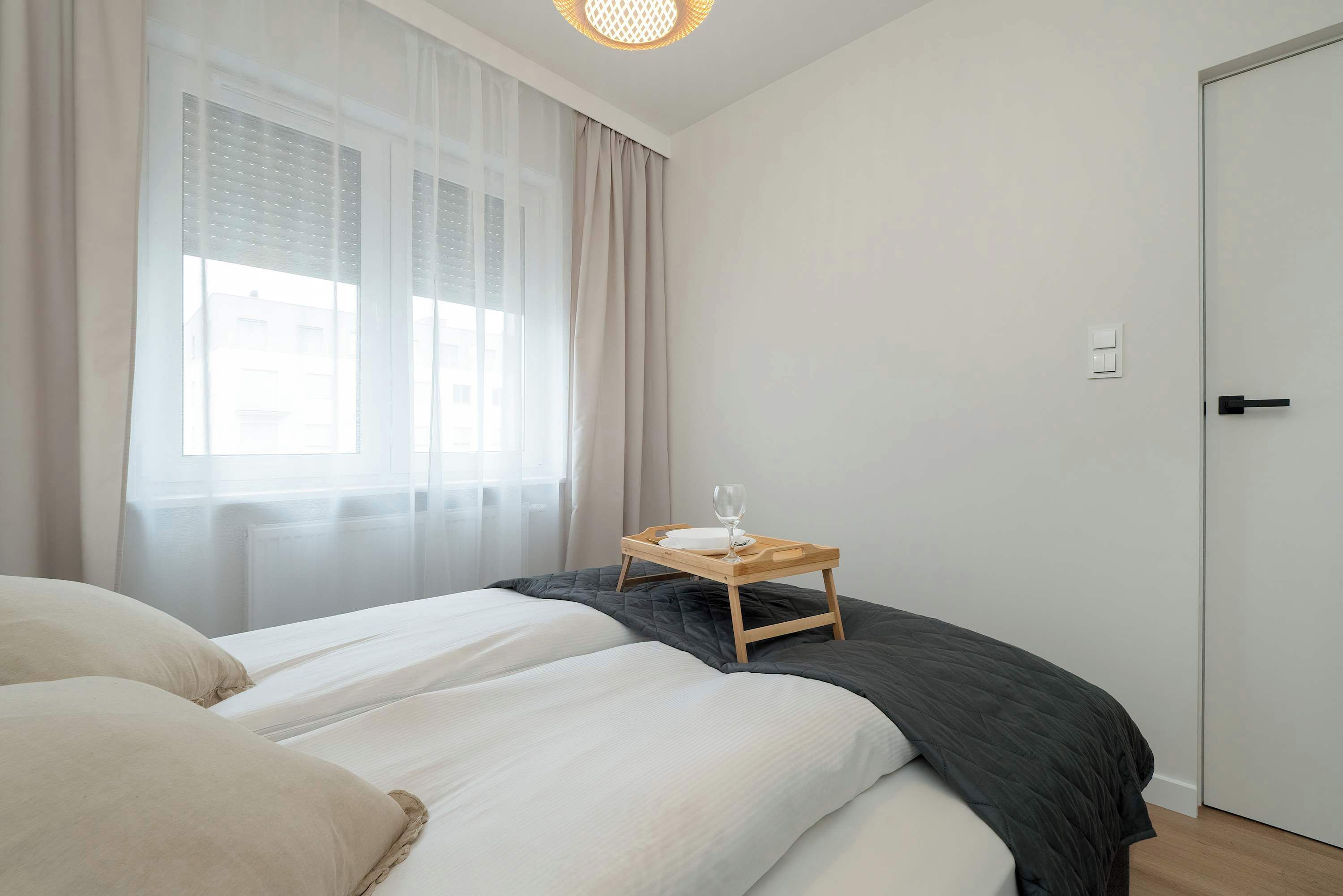 A bedroom with a bed, a bedside table with a glass, and a window with curtains.
