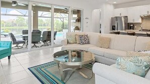 A spacious living area with a white sofa, a glass coffee table, and a dining area with a kitchen in the background.