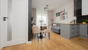 A modern living room with a grey sofa, a dining table with chairs, and a kitchen area with cabinets.