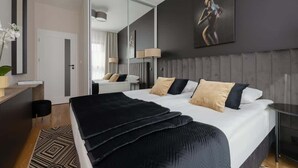A modern bedroom with a large bed, a bedside table, a mirror, and a wall-mounted artwork.