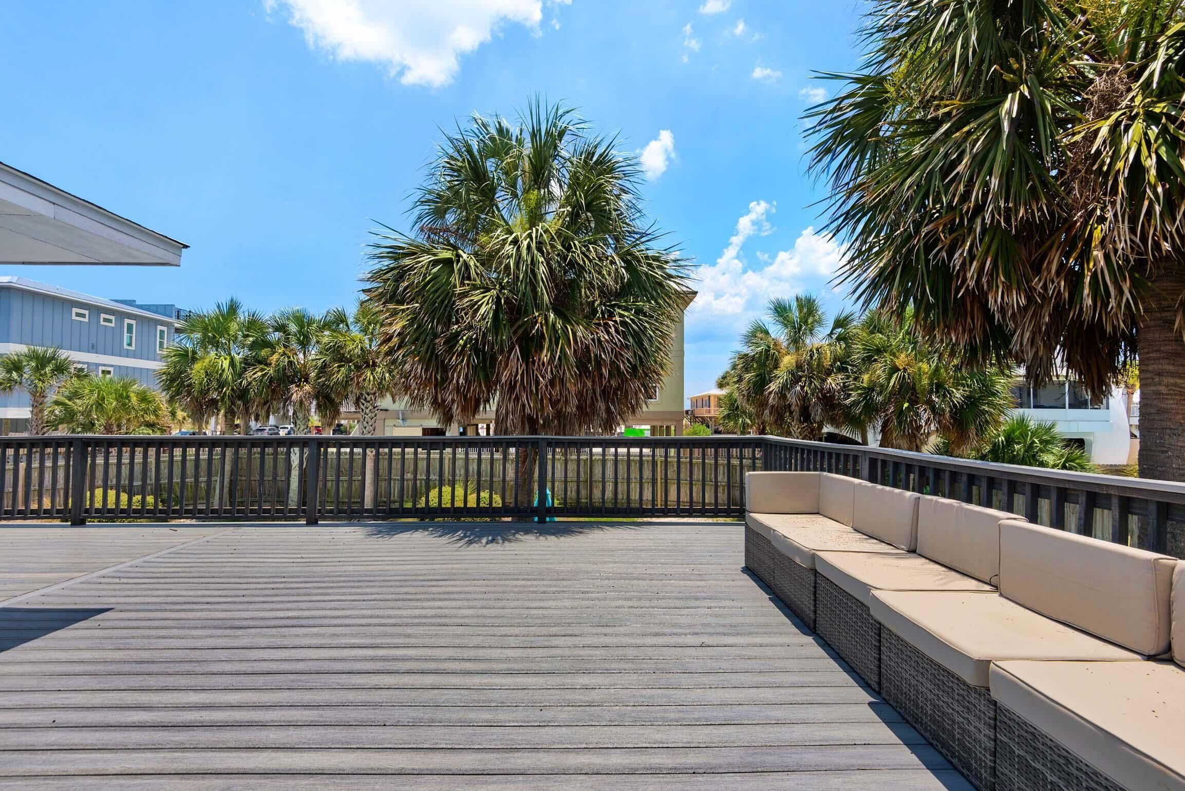 A wooden deck with a black railing and beige cushioned seating.