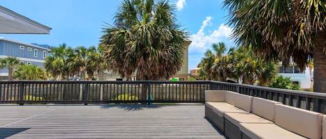 A wooden deck with a black railing and beige cushioned seating.
