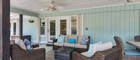 A covered outdoor seating area with wicker furniture, a glass-top coffee table, and ceiling fans.