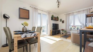 Un salon moderne comprenant un coin repas, un téléviseur et un balcon agrémenté de rideaux.