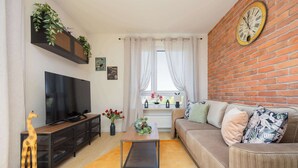 Un salon avec un téléviseur, un canapé, une table basse et un mur en briques.