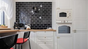 Une cuisine avec des meubles blancs, un plan de travail noir recouvert de carreaux, une machine à café et un four à micro-ondes.