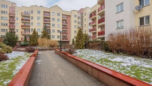 A residential building with multiple balconies, a paved walkway, and snow on the ground.