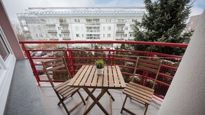 A balcony with a wooden table and chairs, a potted plant, and a red railing.