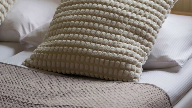 A bed with a knitted blanket and two textured pillows.