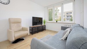 A modern living room with a beige armchair, grey sofa, and a black entertainment unit with a TV.