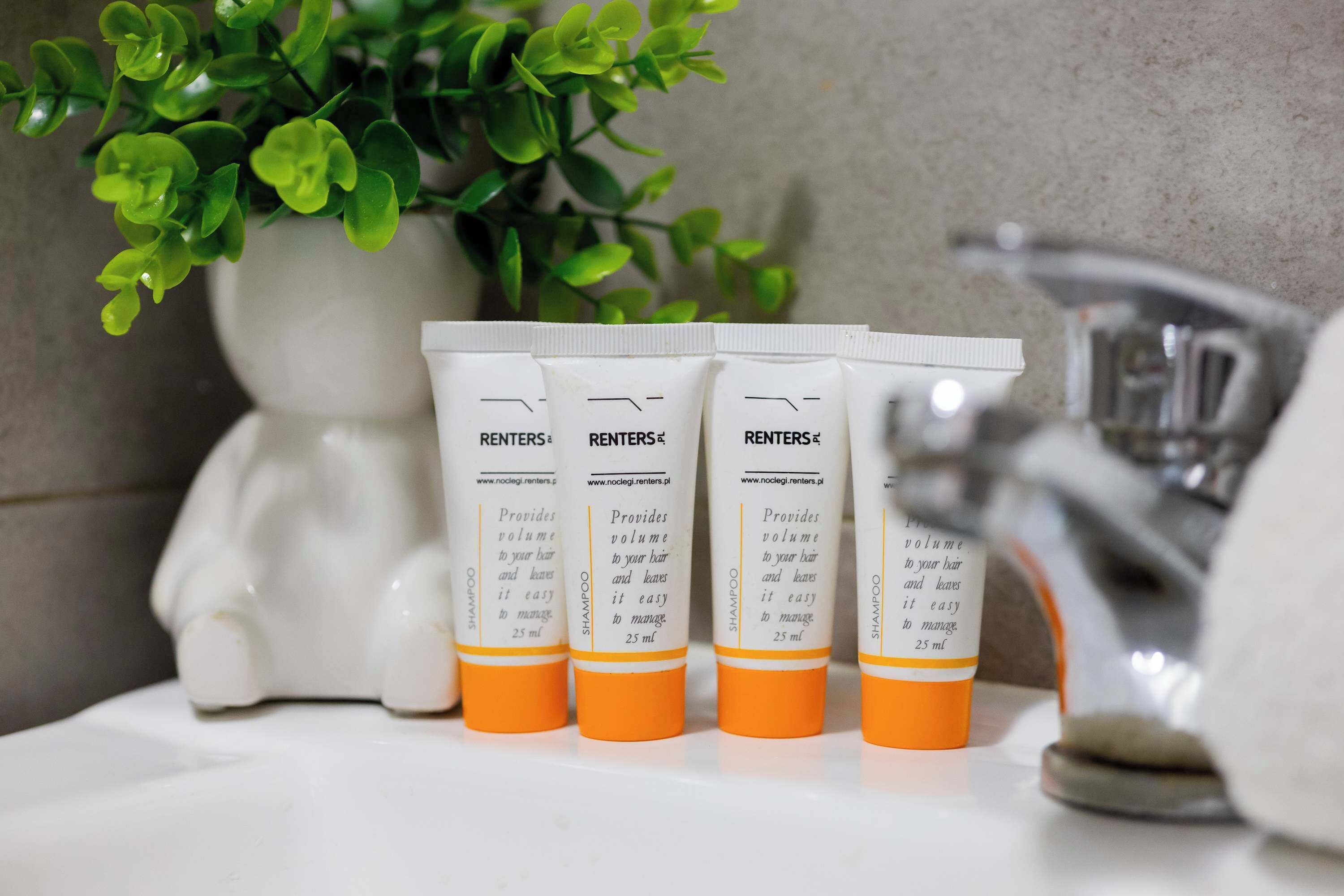 Fire flasker RENTERS® shampoo på en badeværelseshylde med en plante og en hvid keramisk gris i baggrunden.