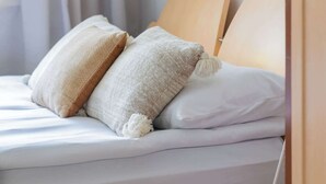 A neatly made bed with white bedding and two pillows, a wooden headboard, and a white floor lamp.