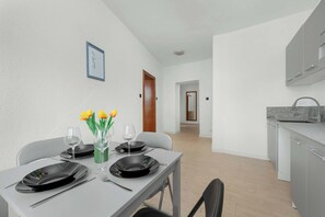 Een moderne keuken met grijze kastjes, een eettafel gedekt met zwarte borden en wijnglazen, en een vaas met gele tulpen.
