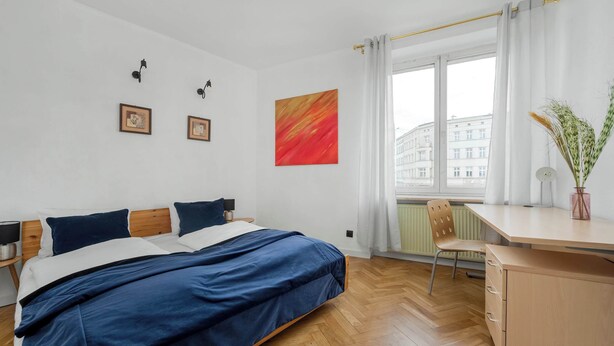 A bedroom with a bed, a desk, and a window.