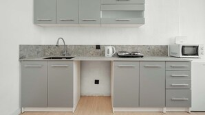 A modern kitchen with grey cabinets, a sink, a kettle, a microwave, and a stove.