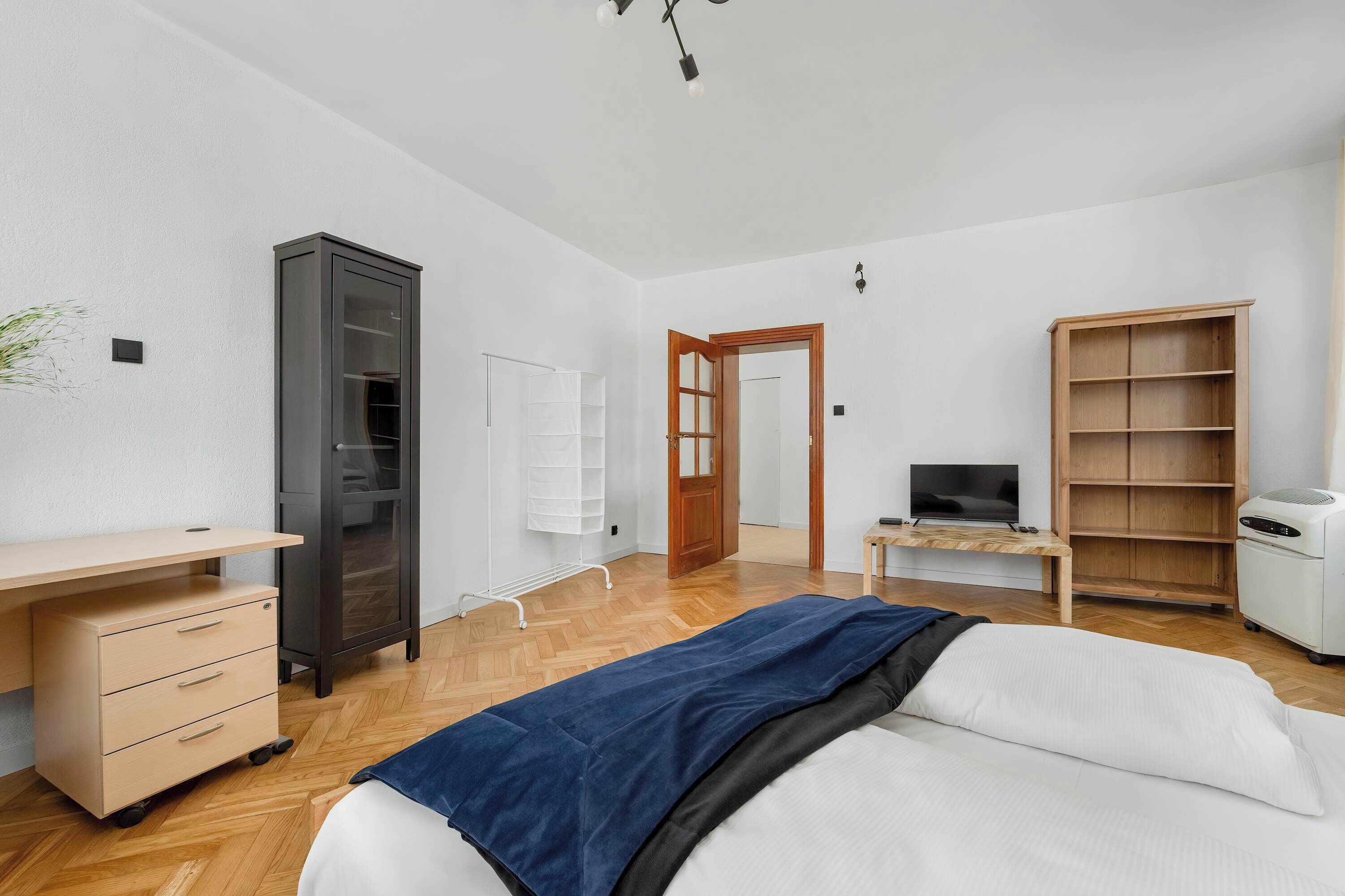 A bedroom with a bed, a desk, a wardrobe, a television, and a heater.