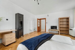 Een slaapkamer met een bed, bureau, kast, televisie en een verwarming.