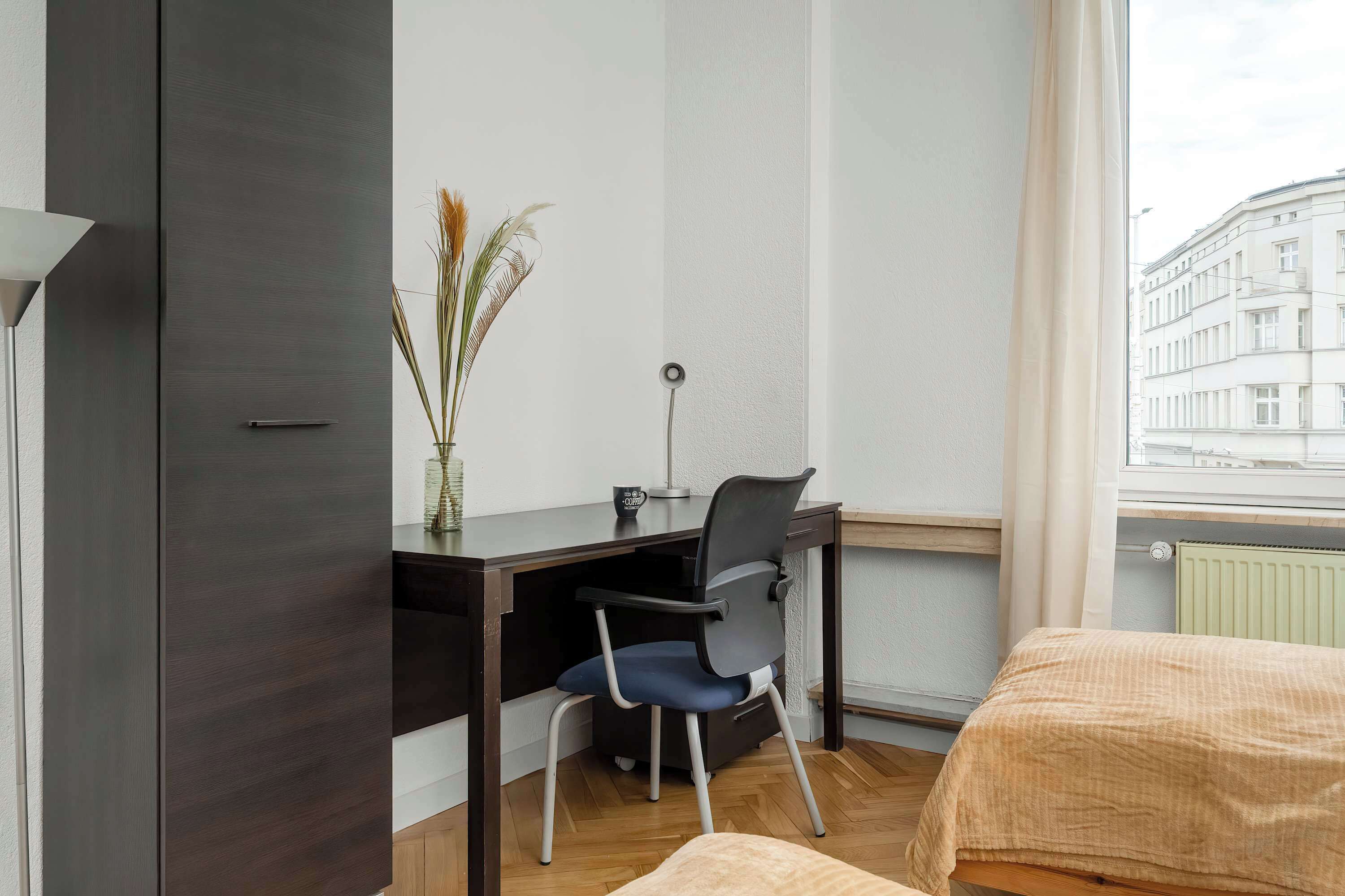 Habitación de hotel con escritorio, silla y vista a un edificio a través de una ventana.