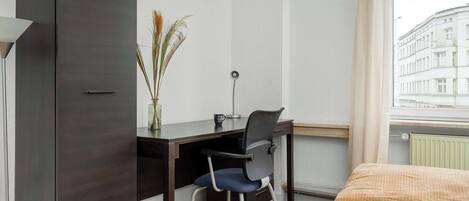 Habitación de hotel con escritorio, silla y vista a un edificio a través de una ventana.