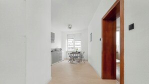 A hallway with a dining area, kitchen, and a view of the outside.
