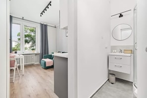 A modern room with a window, a sofa, a small table, and a bathroom with a mirror and sink.