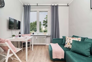 A room with a dining table, a green sofa, a TV, and a window with curtains.