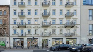 Un immeuble à plusieurs étages, doté de balcons, de devantures de magasins et de voitures garées.