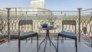 Un balcon avec deux chaises et une petite table, une rambarde décorative en métal et une vue sur un bâtiment en arrière-plan.
