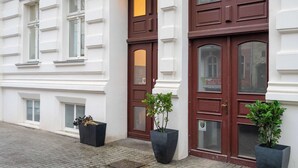 Un edificio con paredes exteriores blancas, dos puertas dobles marrones y dos macetas con plantas en el suelo.