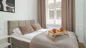 Una cama bien hecha con una bandeja de alimentos para el desayuno, una ventana con cortinas y un cuadro en la pared.