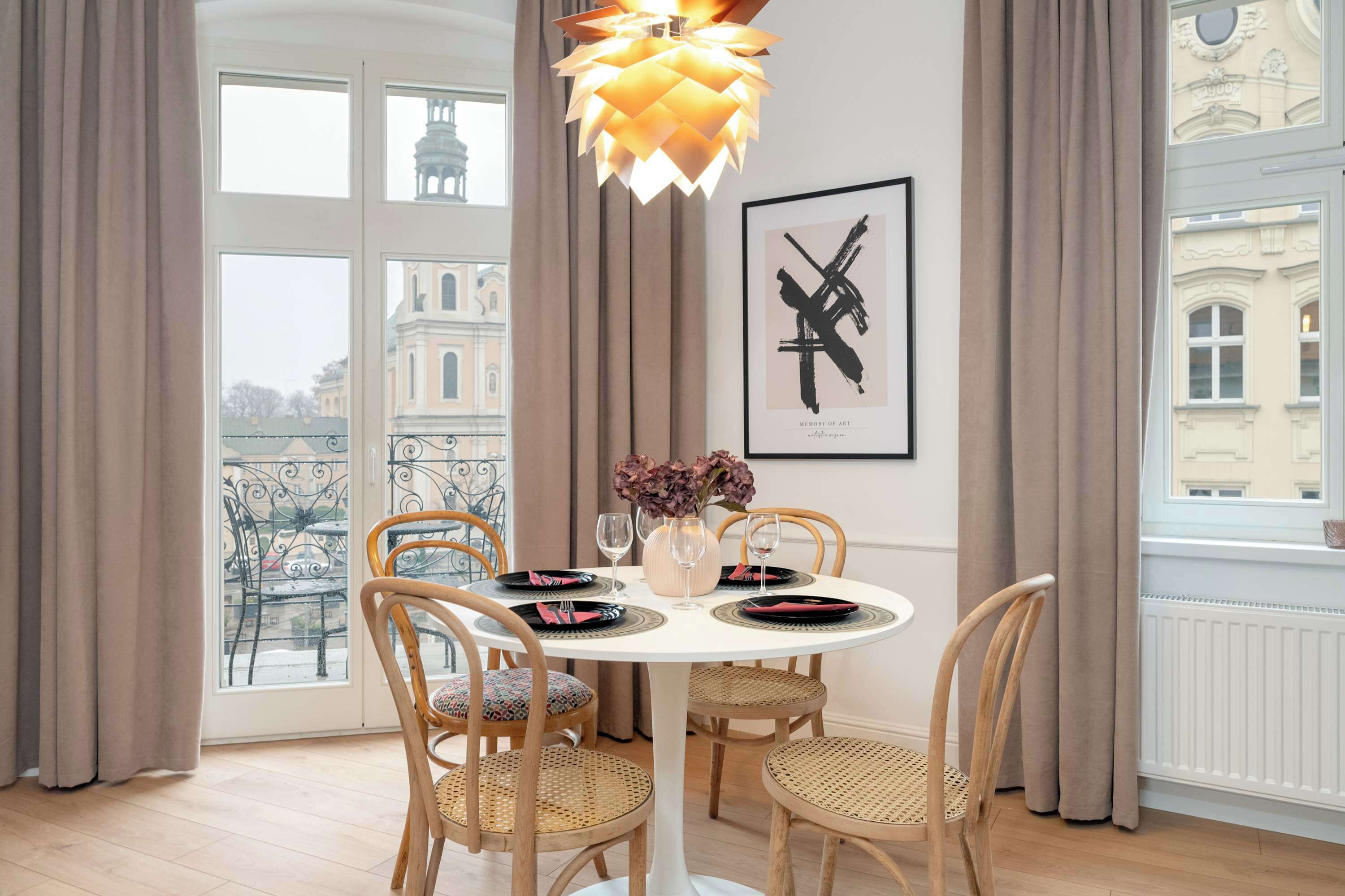 A dining area with a round table, four chairs, a vase with flowers, and a framed artwork on the wall.