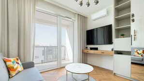 Una sala moderna con un sofá gris, una mesa redonda de centro, un televisor de pantalla plana y un amplio ventanal con vistas a la ciudad.