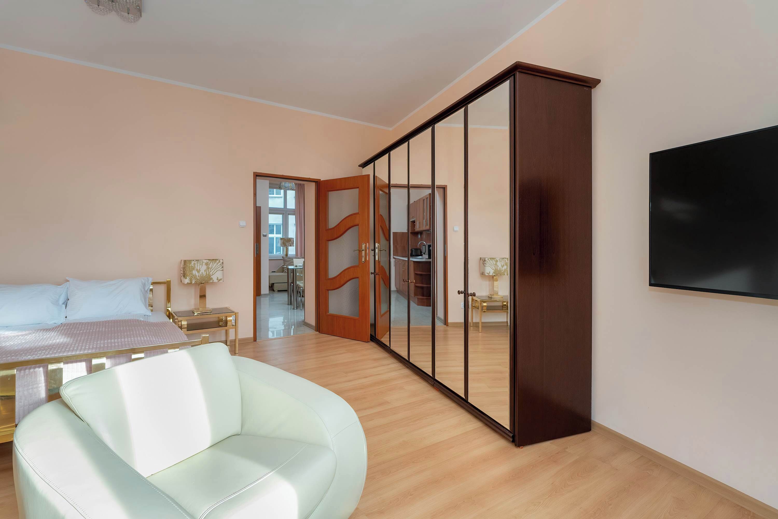 A bedroom with a bed, a white armchair, a wardrobe, and a television.
