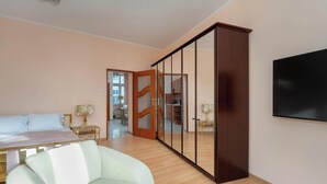 A bedroom with a bed, a white armchair, a wardrobe, and a television.
