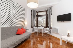 Quarto moderno com sofá cinzento, uma mesinha, televisão e janela com cortinas.