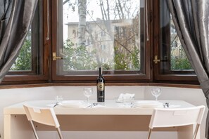 Una mesa de comedor con una botella de vino, copas y vistas a un edificio y árboles por la ventana.