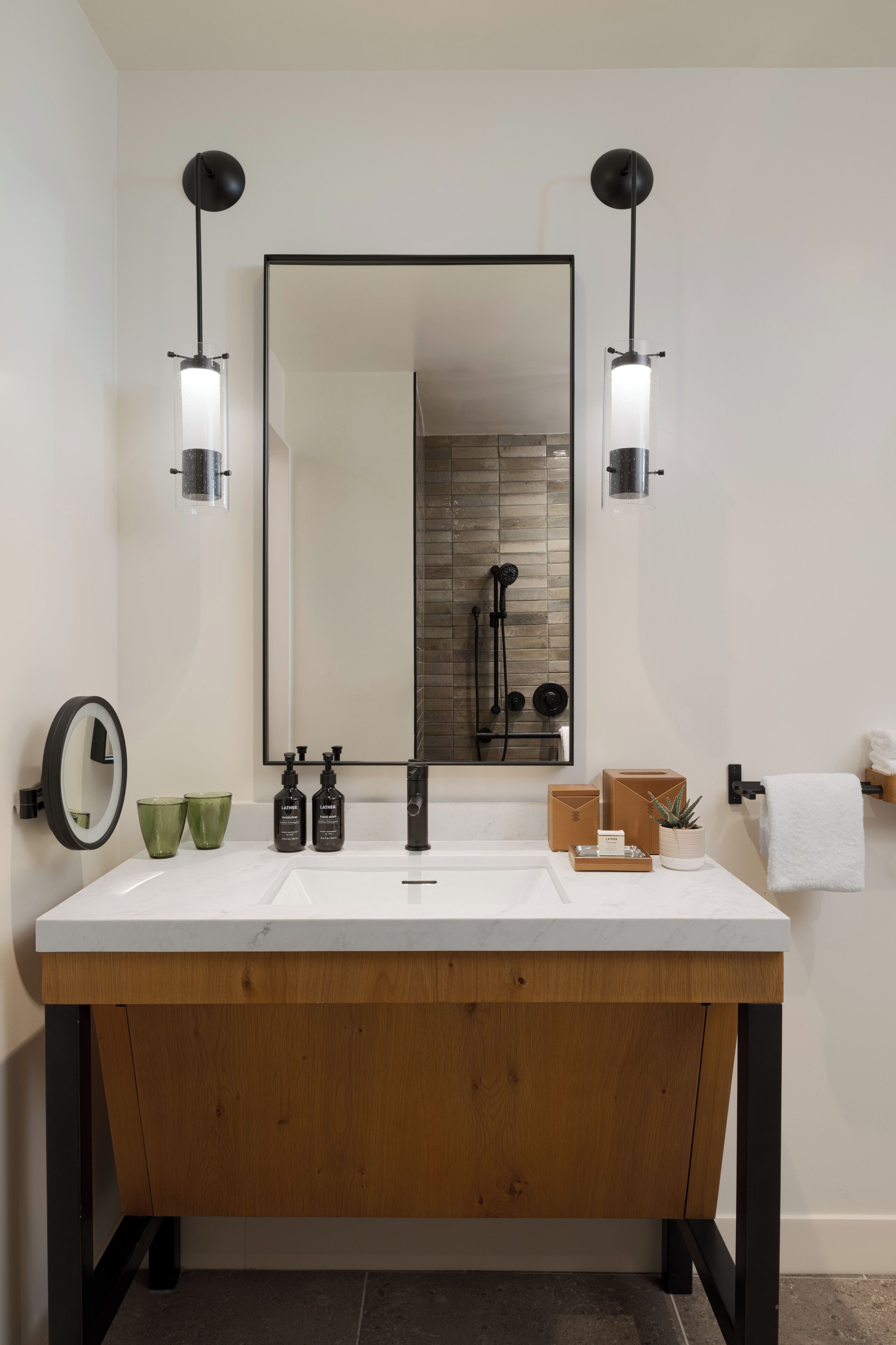 A modern bathroom with a large mirror, two wall-mounted lights, a wooden vanity, and a towel rack.