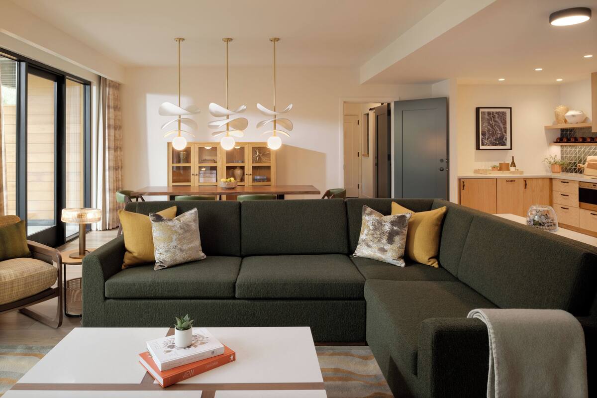 A modern living room with a green sofa, a dining area with a wooden table, and a kitchen with wooden cabinets.