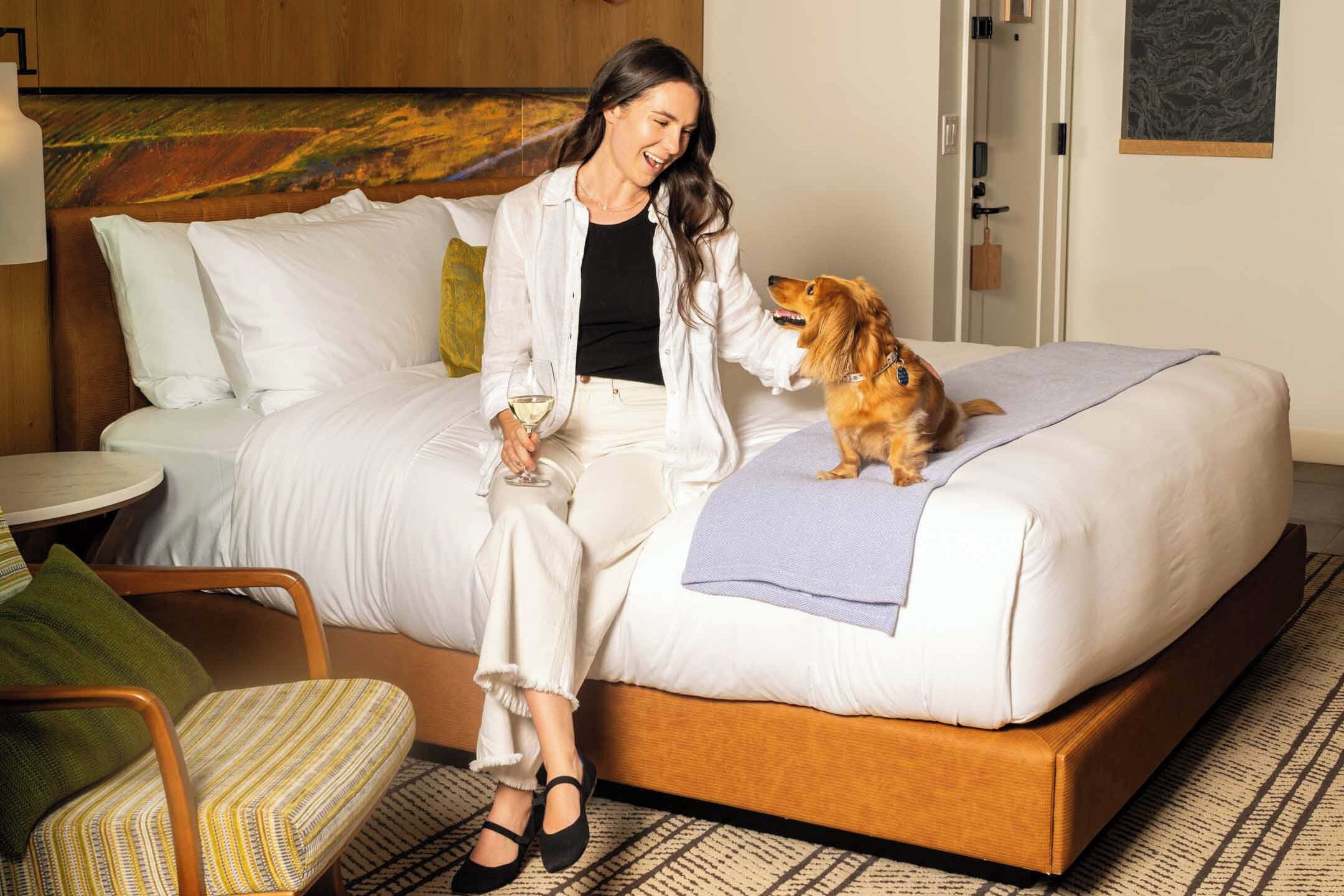 A hotel room with a bed, a chair, a table, and a painting on the wall.