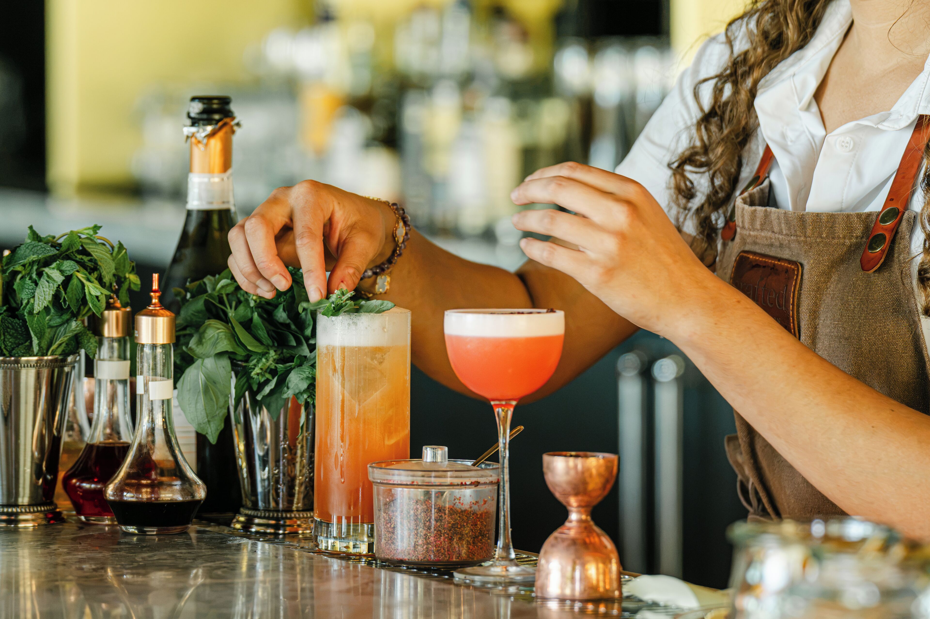 A bar setting with a bartender preparing drinks, various bottles, and a copper shaker.