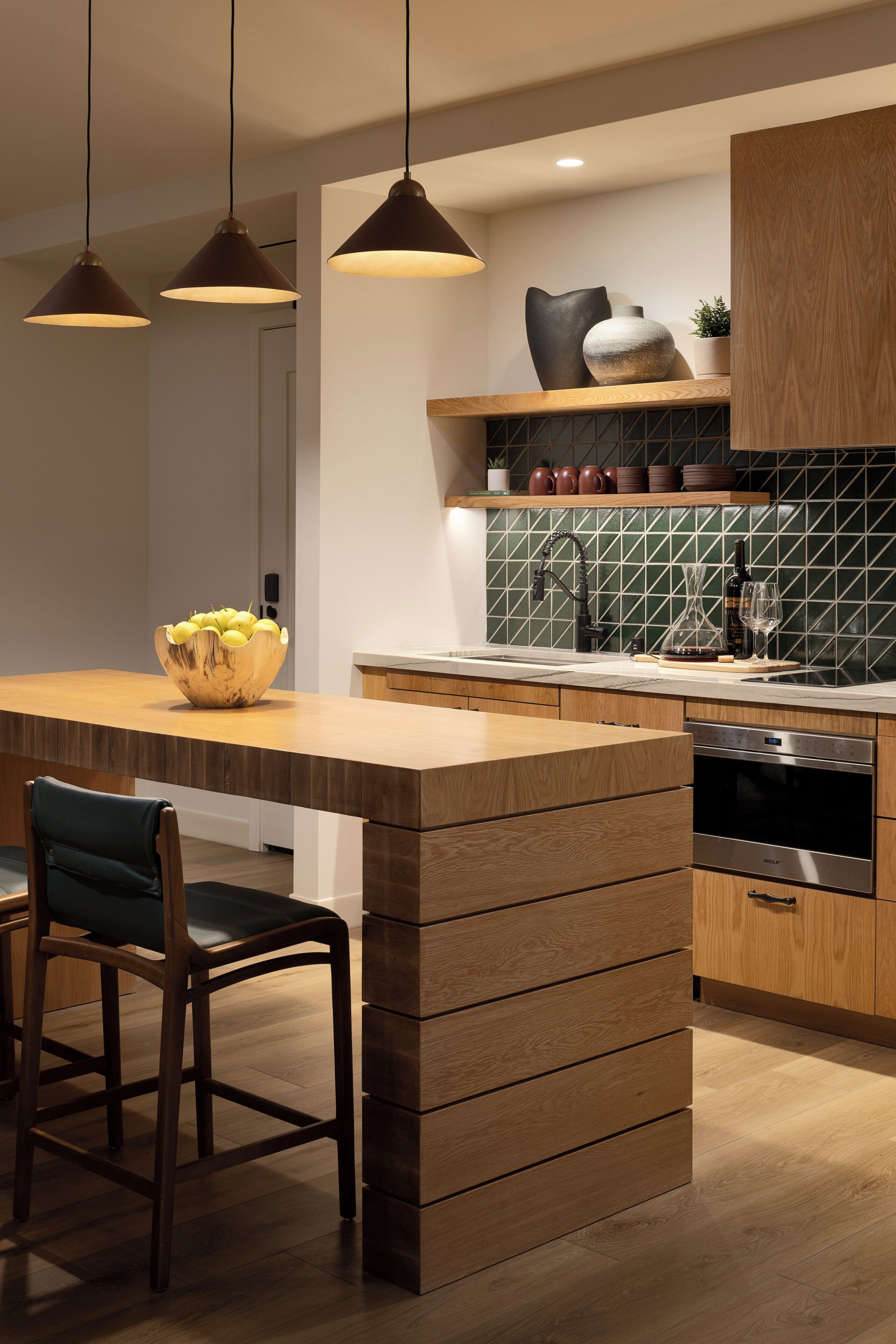Une cuisine moderne avec un îlot central en bois, des luminaires suspendus et un revêtement mural en carreaux.