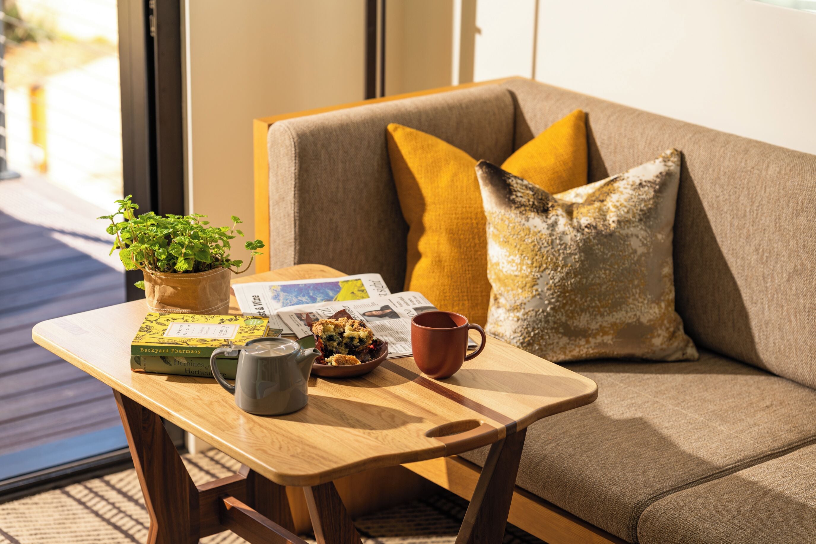A cozy seating area with a sofa, a wooden table, a potted plant, a book, a mug, and a newspaper.