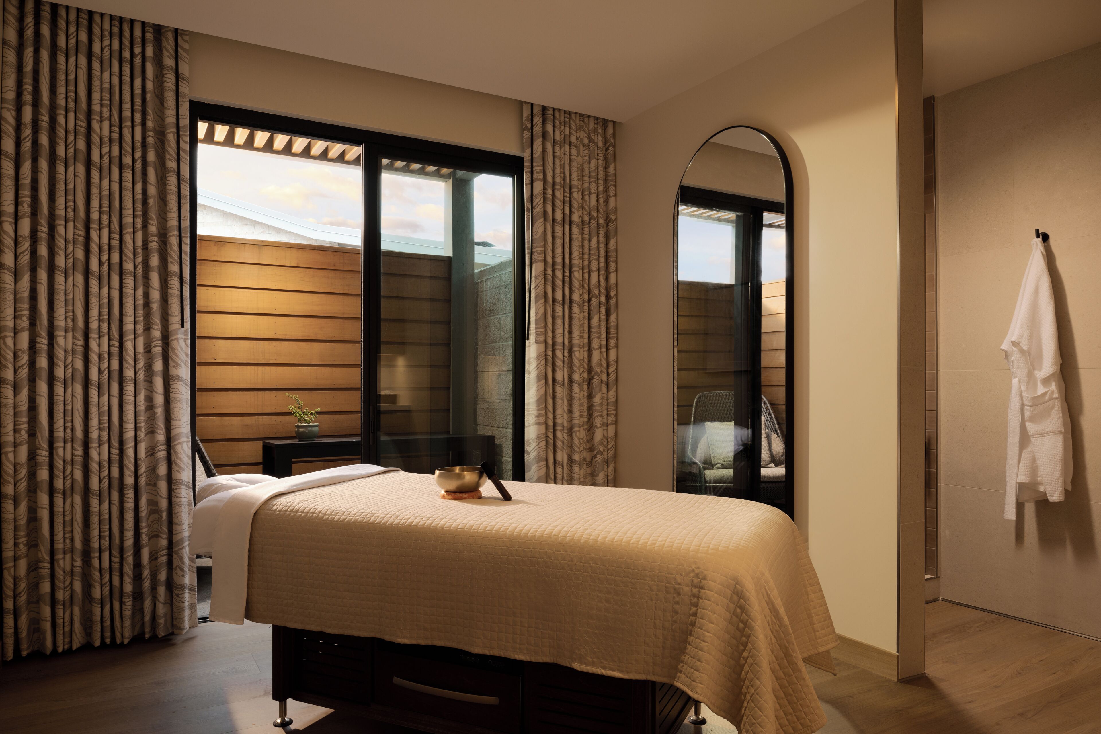 Une chambre à coucher avec un lit, une table de chevet, une fenêtre avec des rideaux, un miroir et une serviette accrochée au mur.