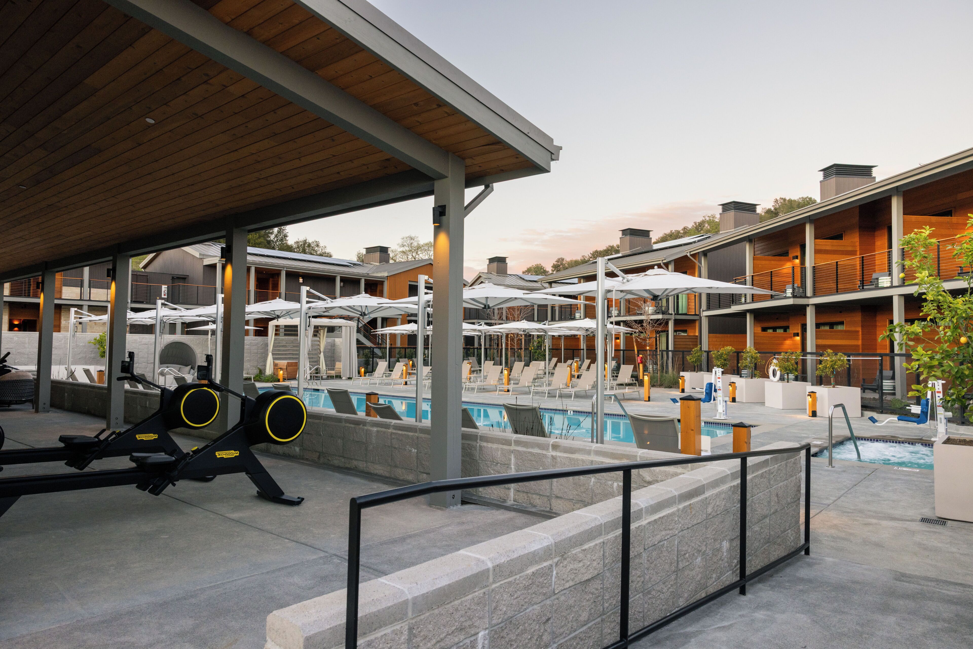 Zona de piscina con sillones reclinables, terraza de madera y equipo de ejercicio.