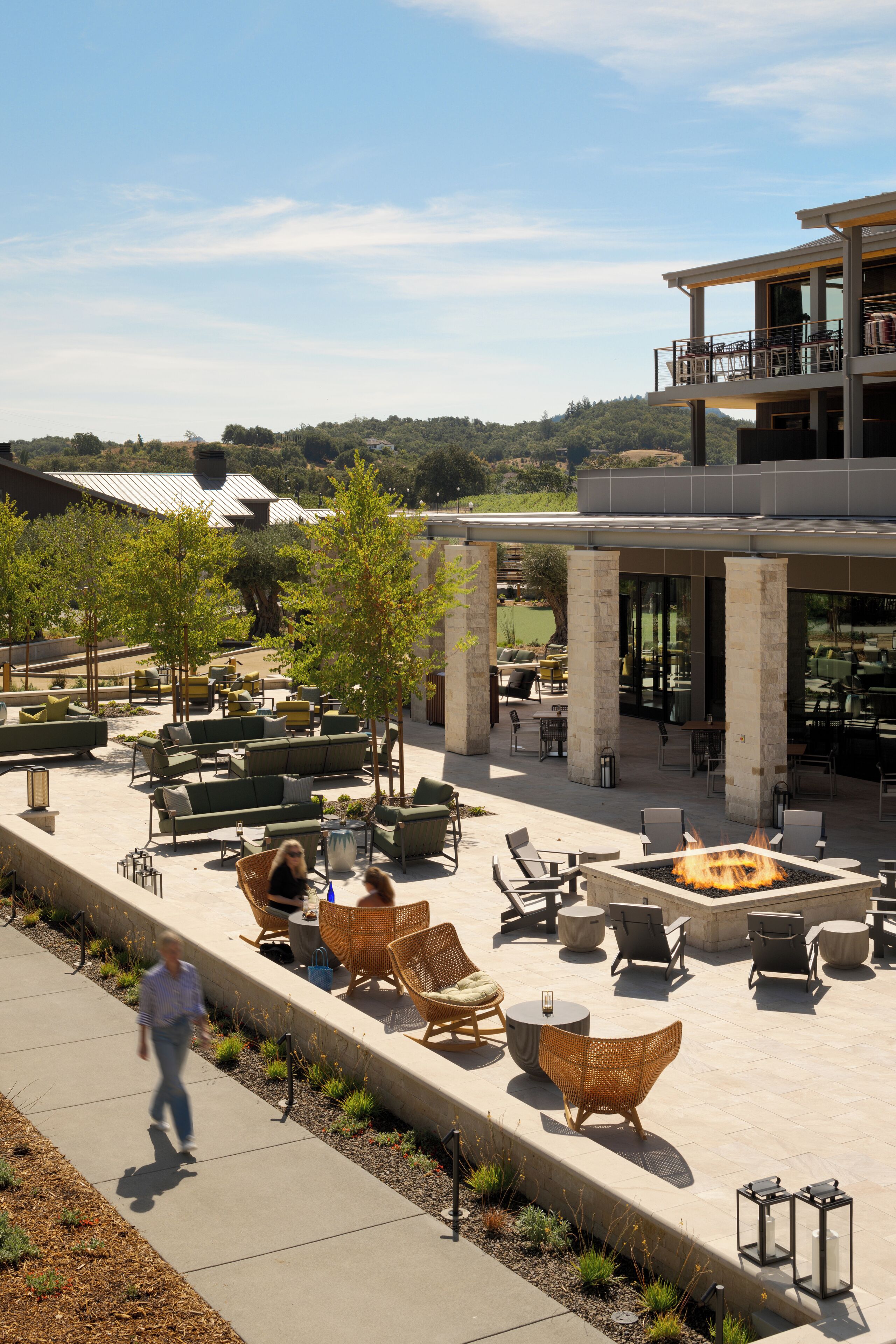 An outdoor patio area with multiple seating arrangements, including sofas and chairs, and a central fire feature.