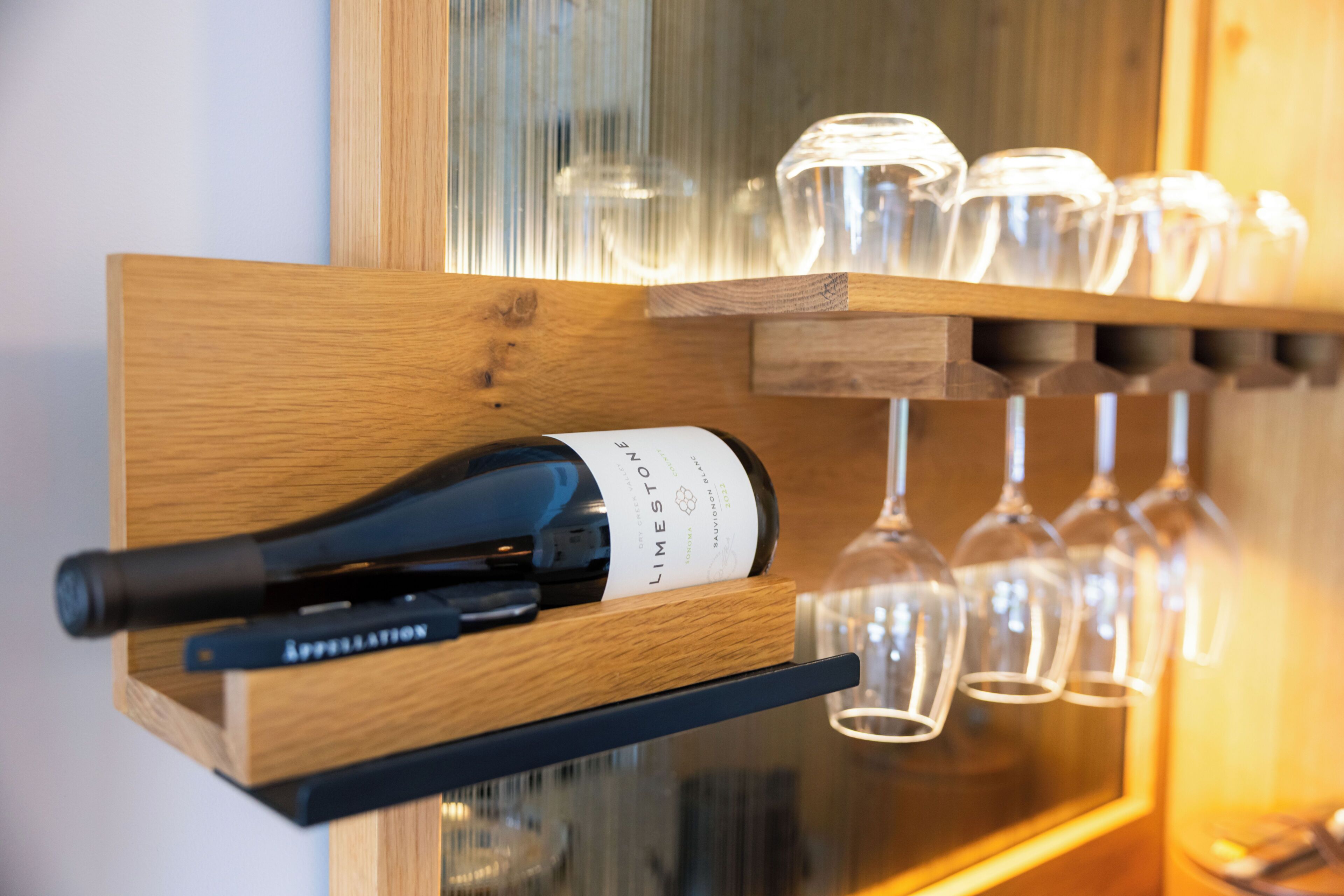 A wine bottle on a wooden rack with several wine glasses hanging above.